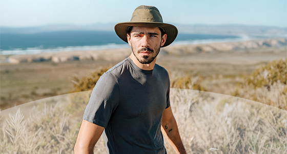 Man in Tilley hat with large shore in the background looking into the distance. 