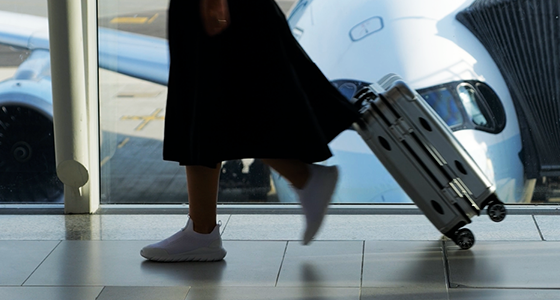Image showing woman walking at an airport, rolling her carry-on with plane parked at a gate.