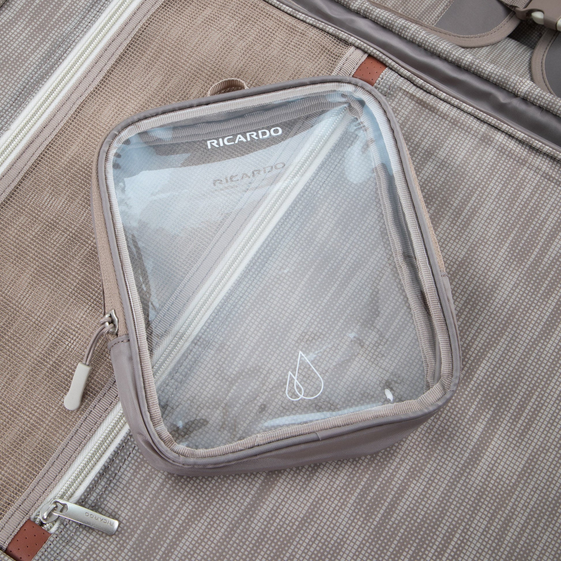 A clear pouch labeled "RICARDO" rests on a Ricardo Beverly Hills Montecito 3.0 Softside Carry-on lining.