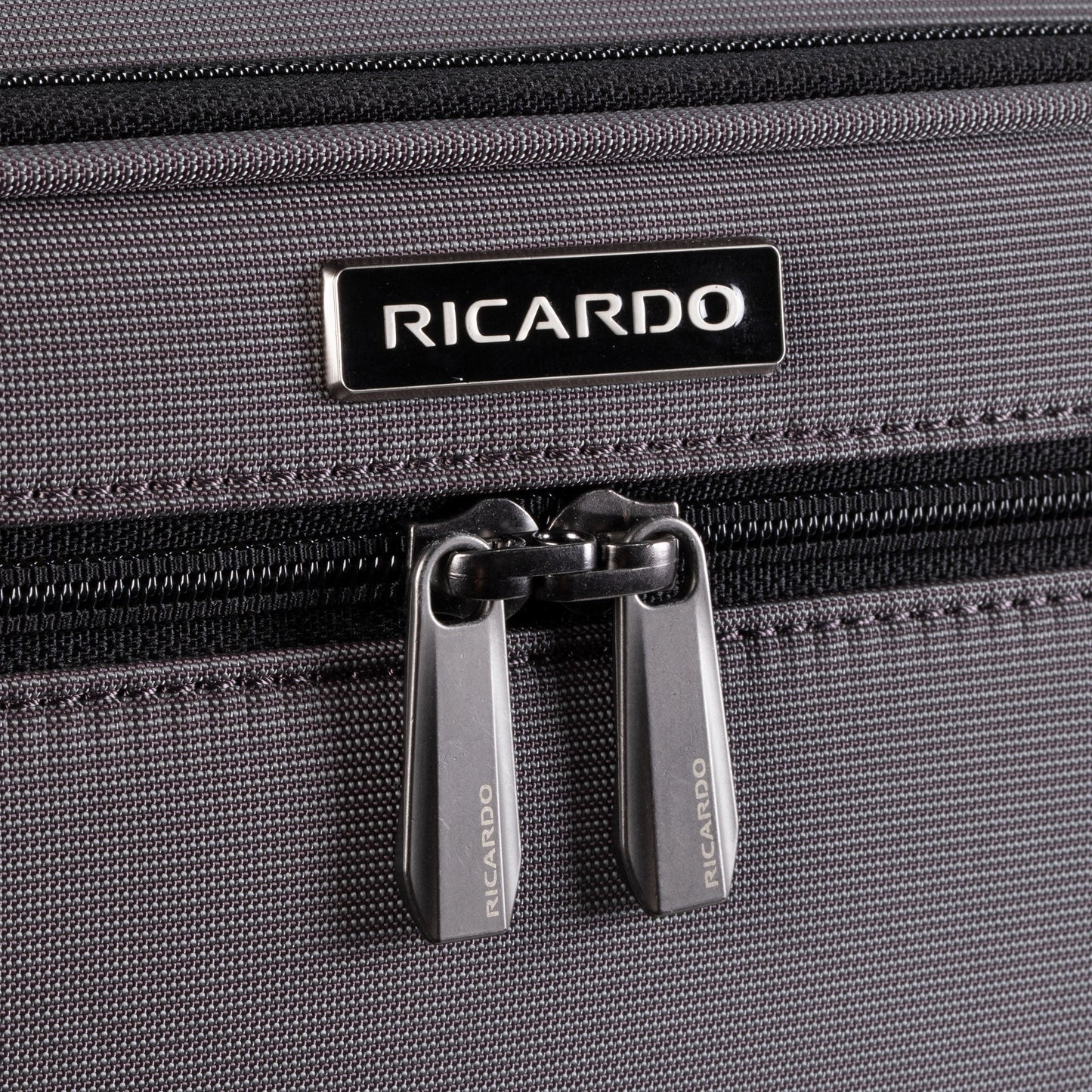 Close-up of Ricardo Beverly Hills Montecito 3.0 Softside Carry-on Spinner in gray with double zippers and logo above.