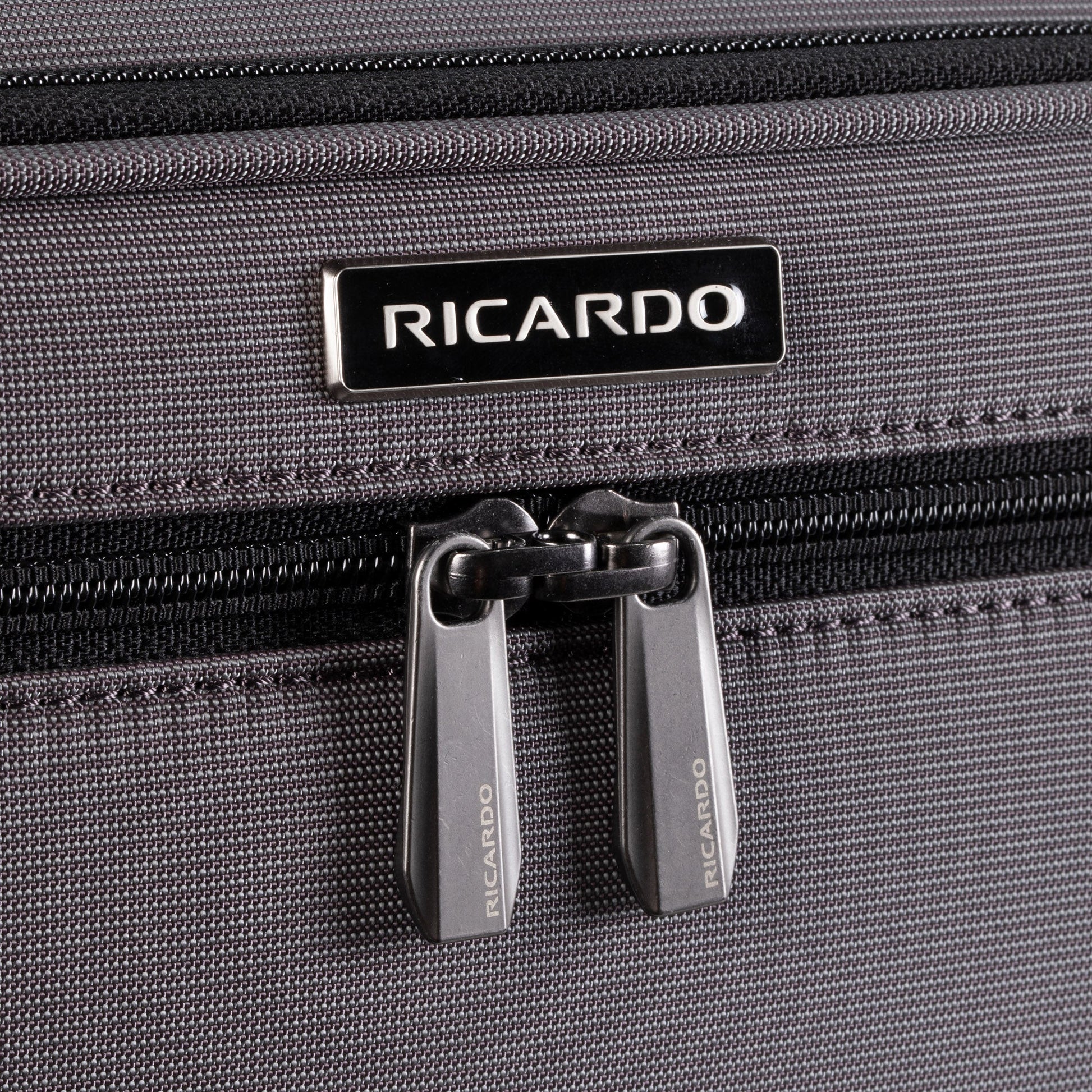 Close-up of Ricardo Beverly Hills Montecito 3.0 Softside Carry-on Spinner in gray with double zippers and logo above.