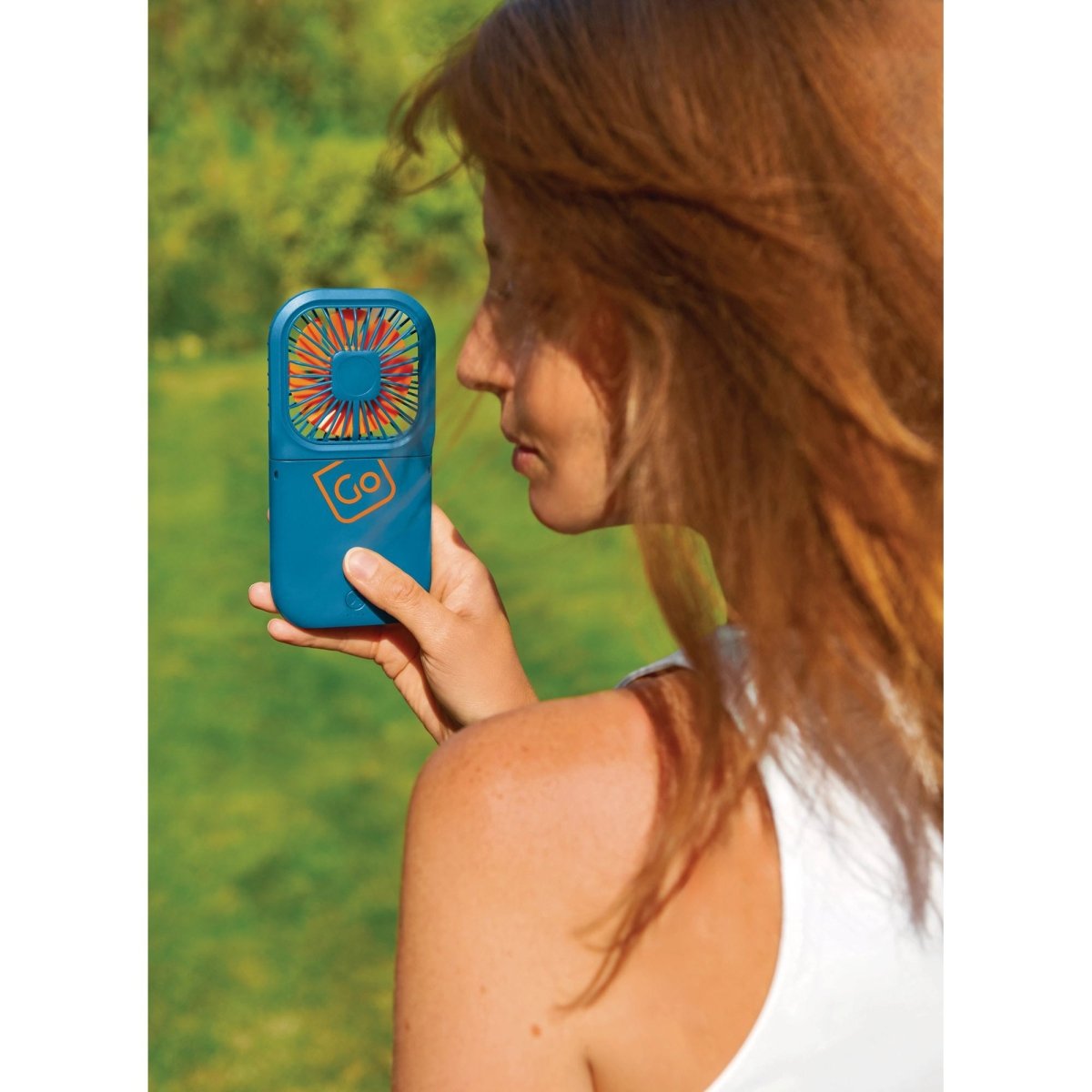 Woman holding Go Travel Flexi Fan outdoors, wind blowing her hair, greenery in the background.