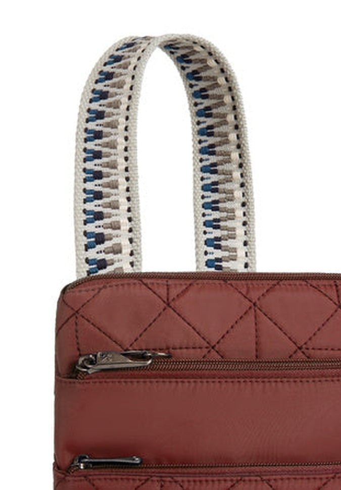 Close-up of the Travelon Boho Anti-Theft Slim Crossbody, a brown quilted bag with a zipper pocket and white handles showcasing a blue pattern, designed in a Boho style.