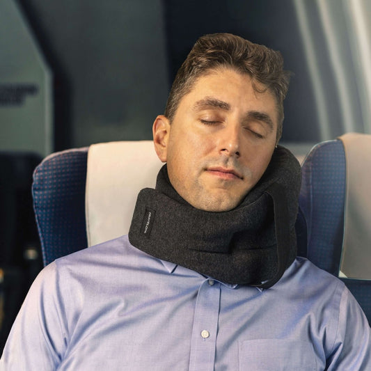 Product Image – A person peacefully sleeping on a plane, nestled in an aisle seat, using a Travelon SOMNiWRAP Travel Pillow in black, designed ergonomically for optimal neck support.