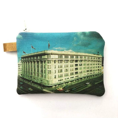 The Winnipeg North of Fargo Coin Purse beautifully features a vintage-style print of a majestic building adorned with columns and flags set against a blue sky, complemented by an interlined design for enhanced durability.